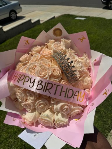 A bouquet of pastel roses with a "Happy Birthday" banner and a silver crown decoration.