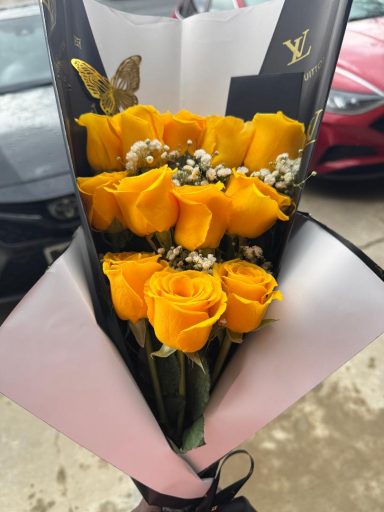 Bouquet of vibrant yellow roses with white filler and green leaves.