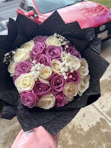 Bouquet of purple and white roses wrapped in black paper.