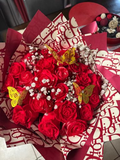 A bouquet of red roses with baby's breath and yellow butterflies on decorative paper.